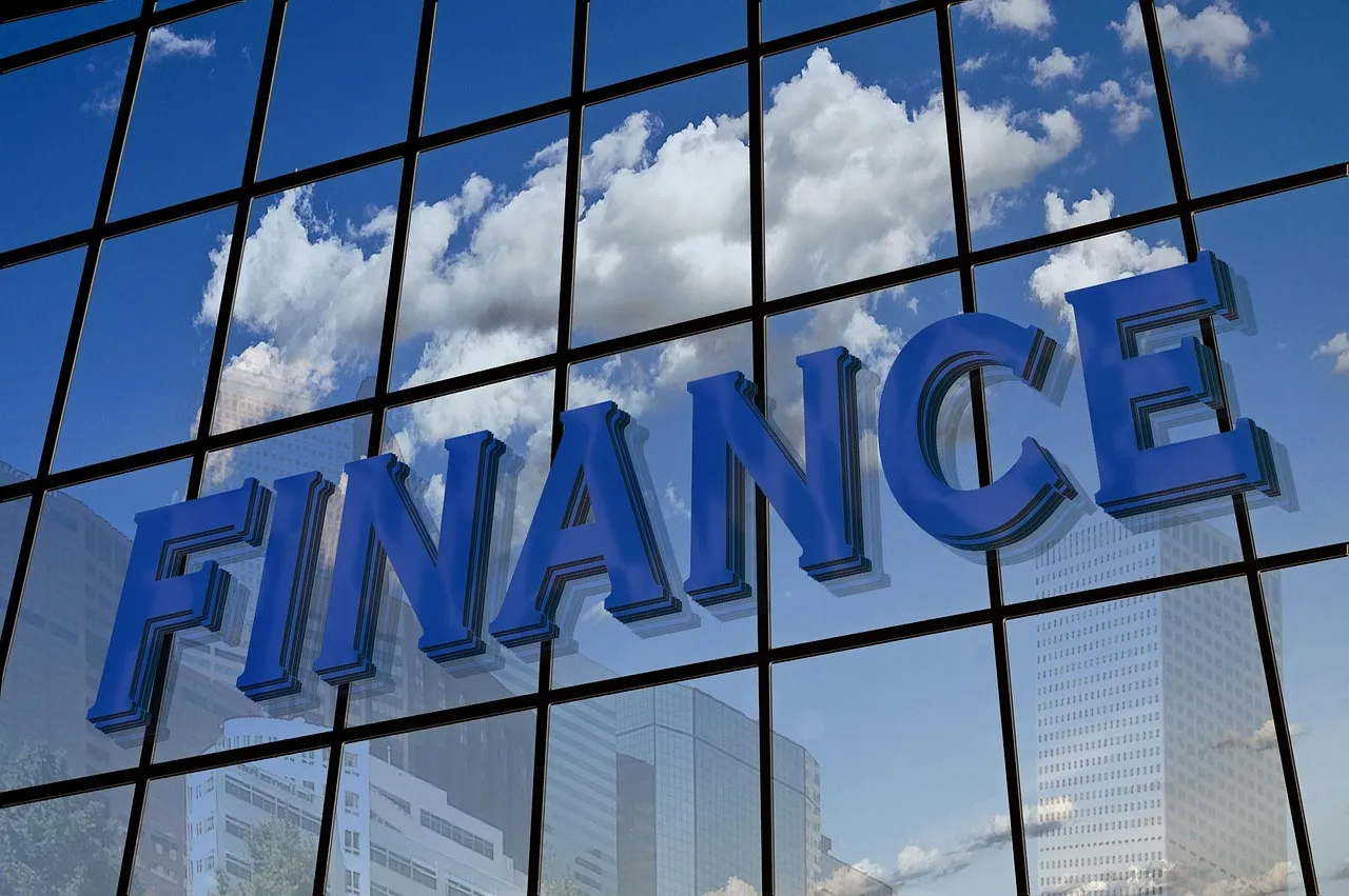 The word FINANCE in large letters on a glass office building facade reflecting clouds and sky.