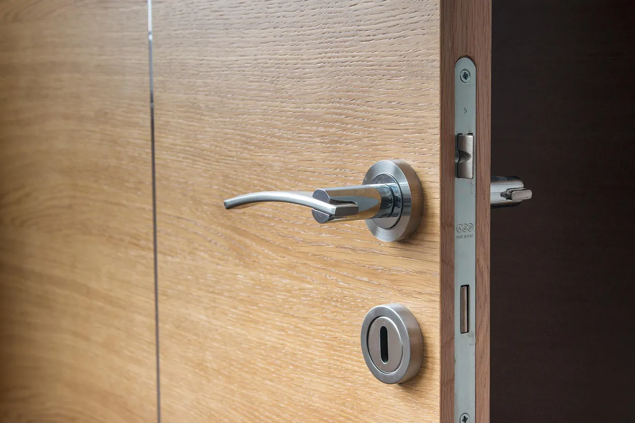 Close view of an open wooden door showing its metal handle, keyhole plate and the latch mechanism in the frame with the bolt withdrawn