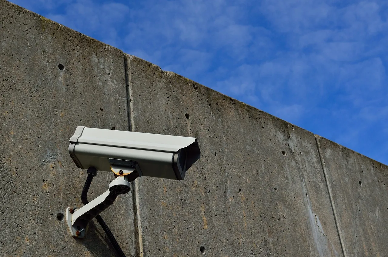 A white CCTV camera mounted on a concrete wall against a blue sky.