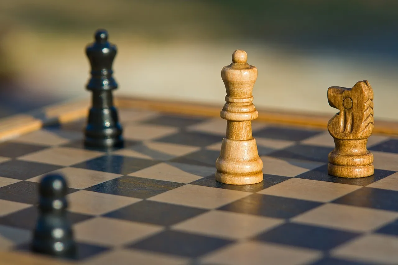 Wooden chess pieces on a board with a dark queen behind and a light queen and knight in front, shot close with the background falling out of focus