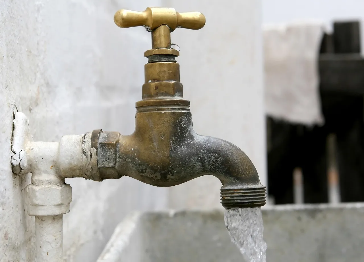 An old brass tap on a white wall with water running from it