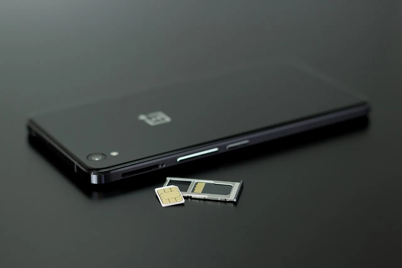 A SIM card resting on its ejected tray beside a black smartphone, gold contacts facing up — the component the researchers treated as the starting point of the attack.