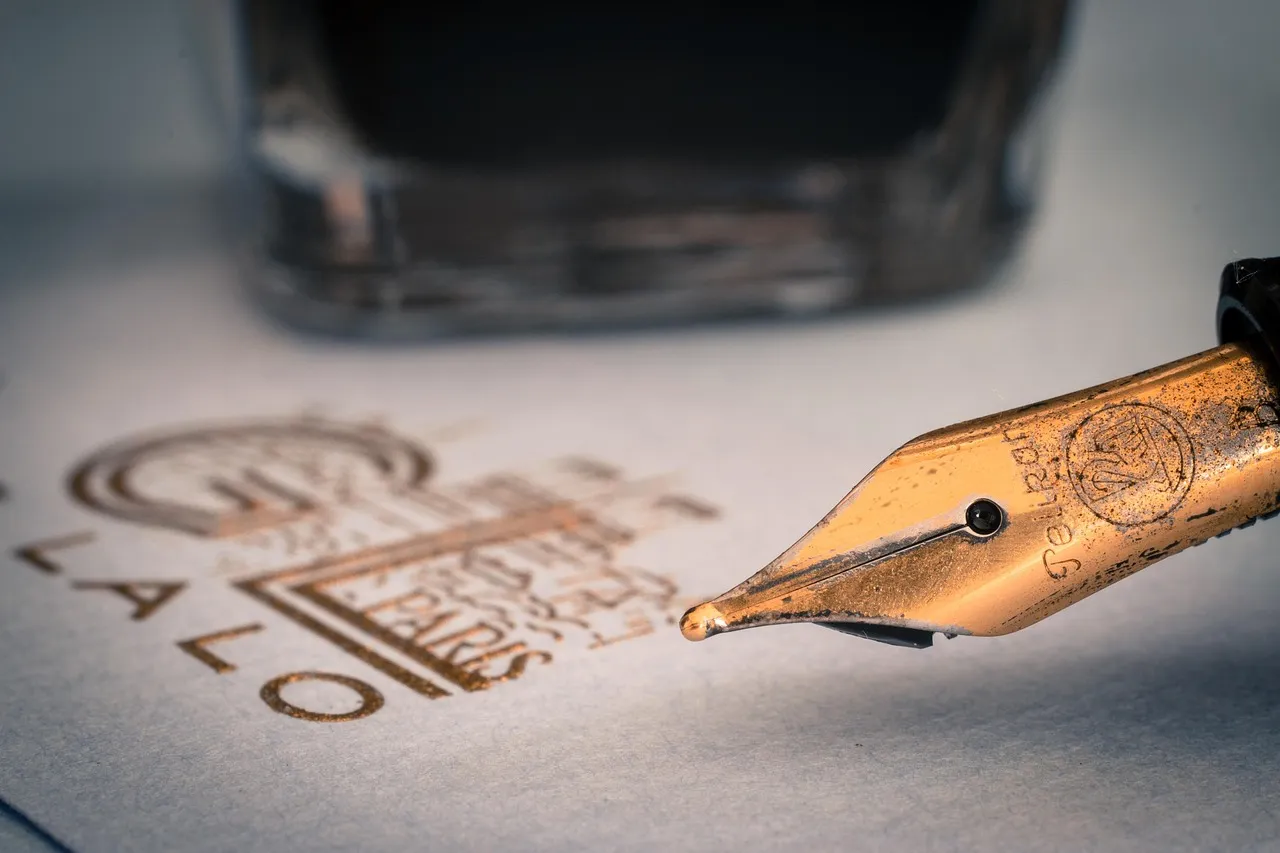 A fountain pen nib resting on paper beside a bottle of ink