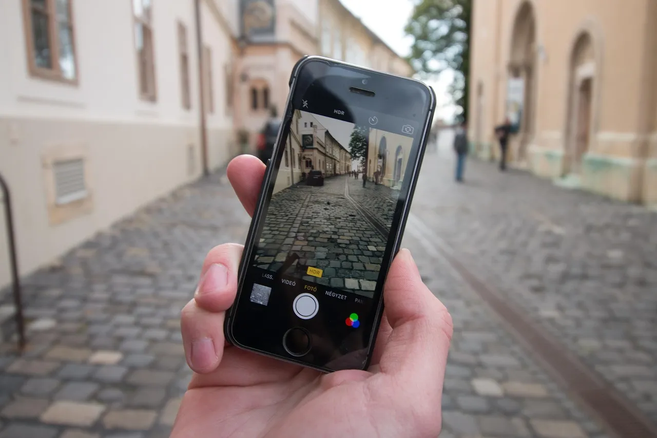 A hand holding a smartphone with the camera open on a cobbled street