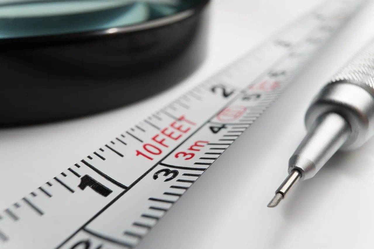 A close-up of a measuring tape marked in centimetres, with a pen tip and a magnifying lens resting beside it