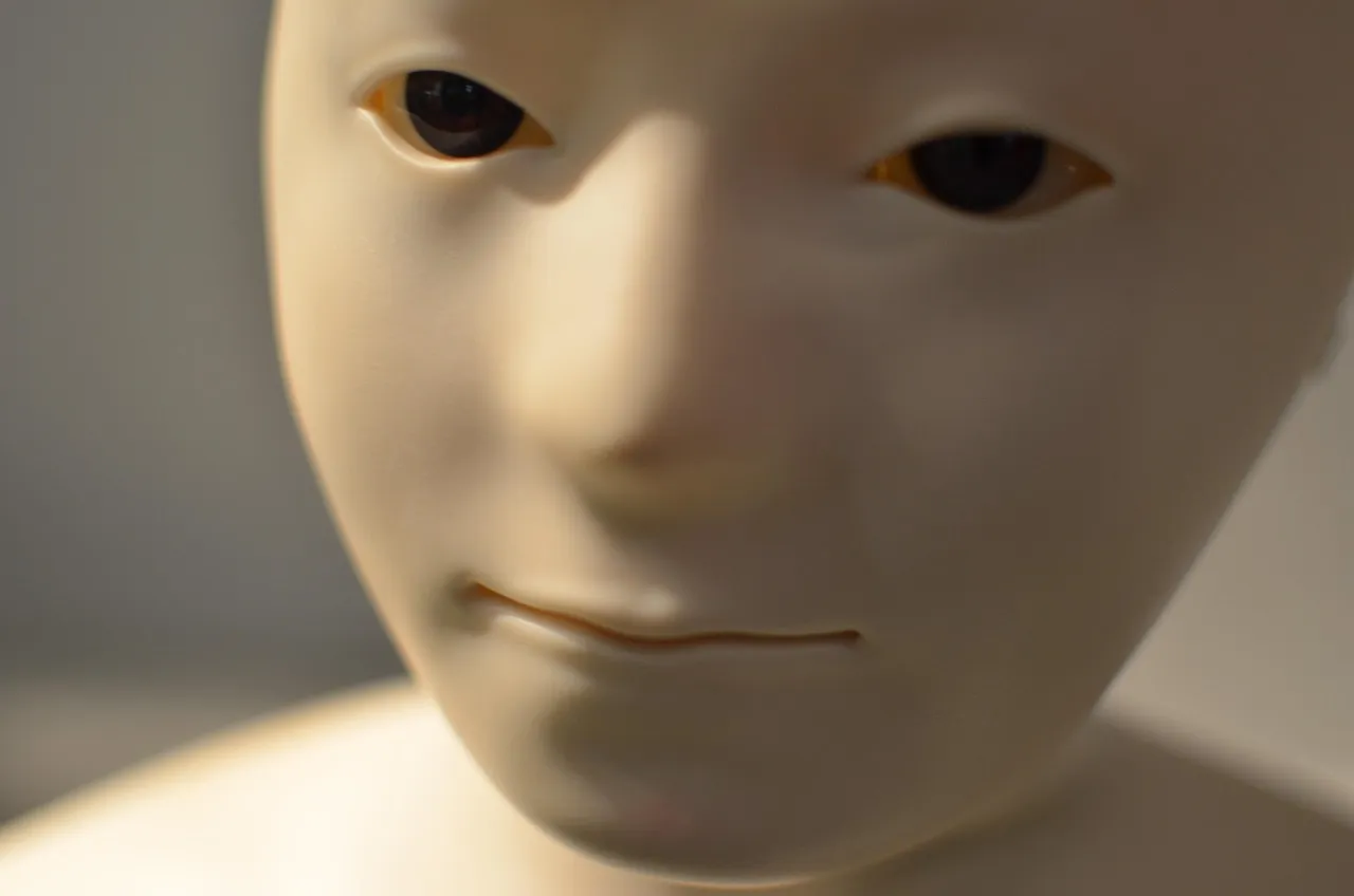 A close-up of a humanoid robot's face moulded in pale plastic, with dark eyes and a fine seam at the mouth.
