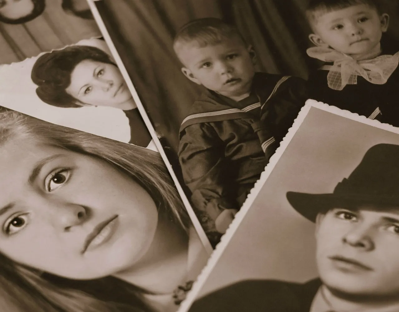 Several old black-and-white family photographs of children and young adults, fanned out on a surface.