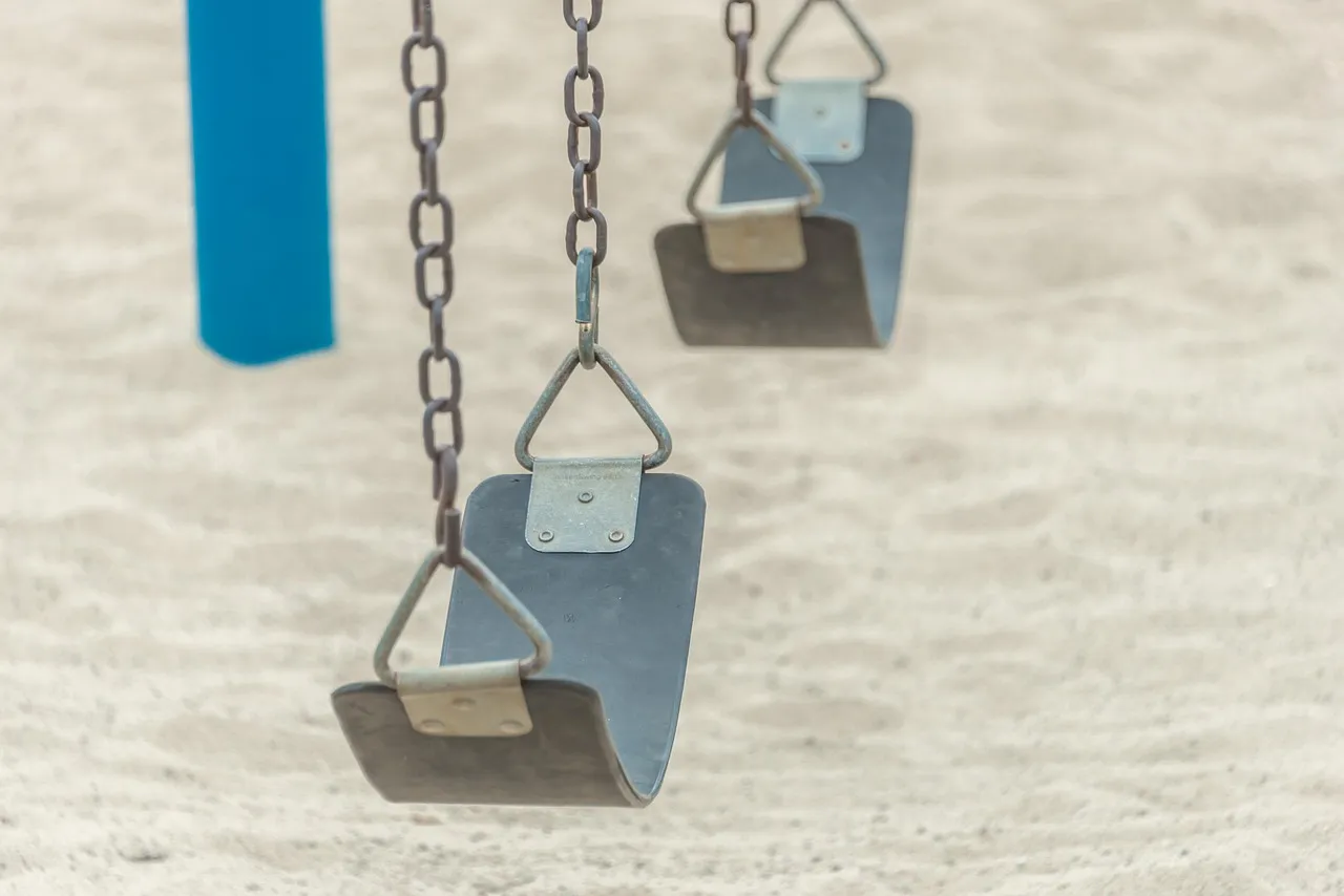 Two empty playground swings hanging still over pale sand