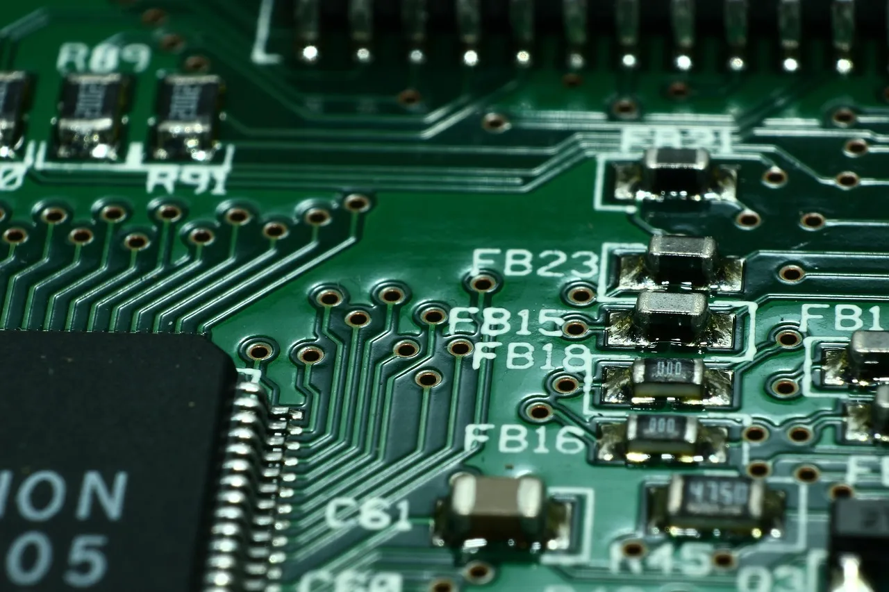 A macro photograph of a green printed circuit board showing surface-mount components and silkscreen reference labels.