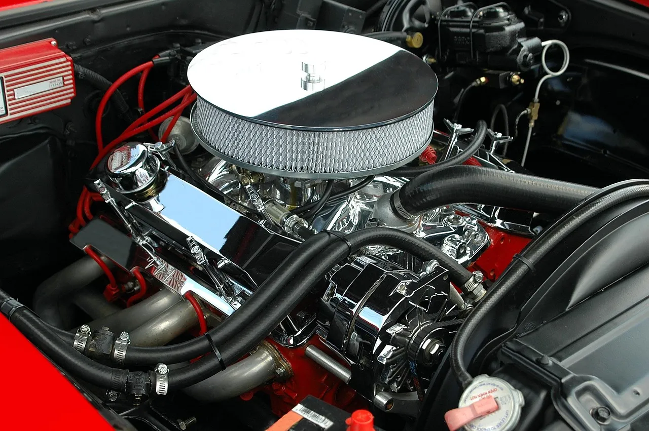 A chrome V8 engine with a round air filter, set in a red engine bay