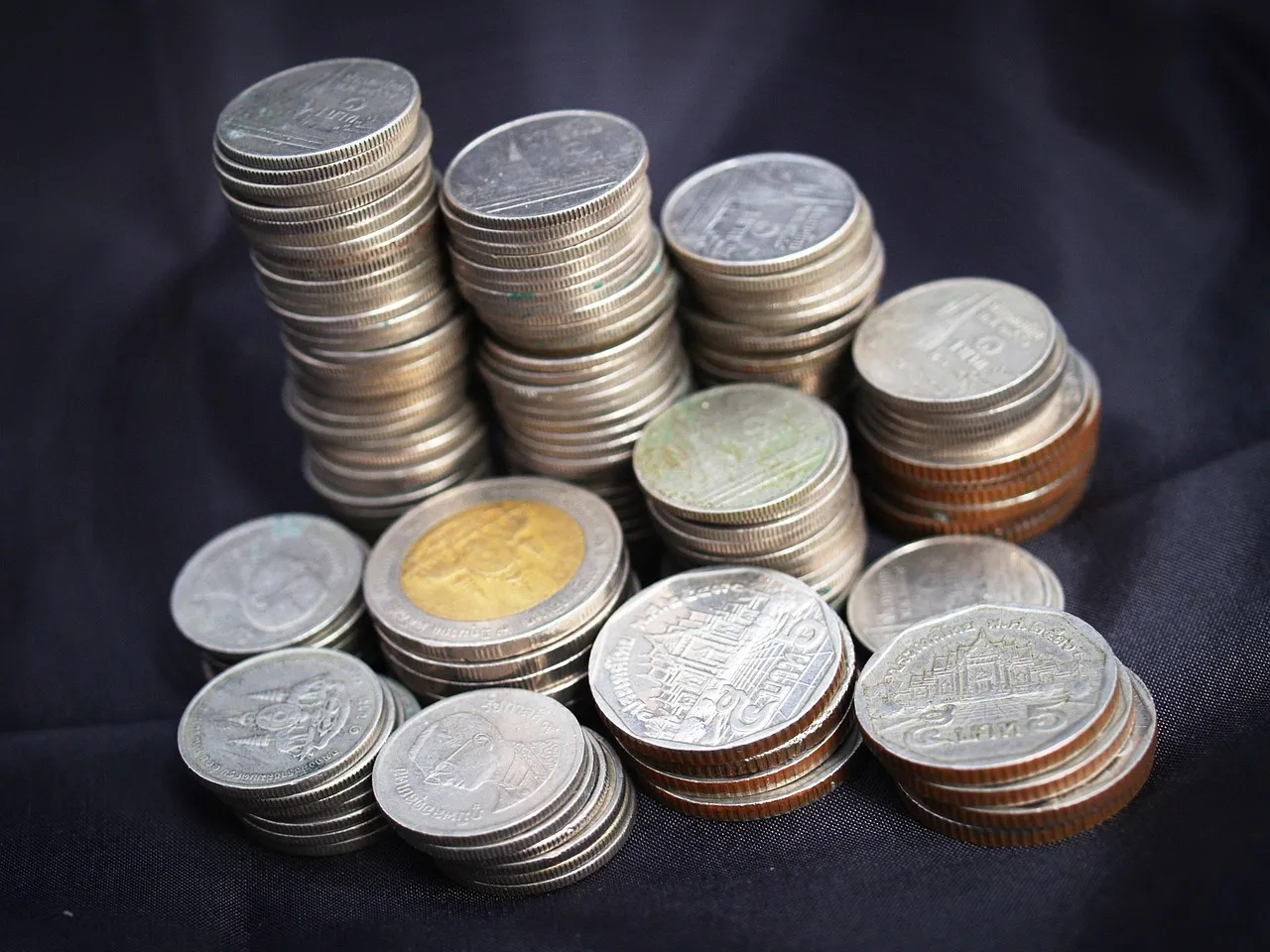 Stacks of silver and two-tone coins on a dark surface.