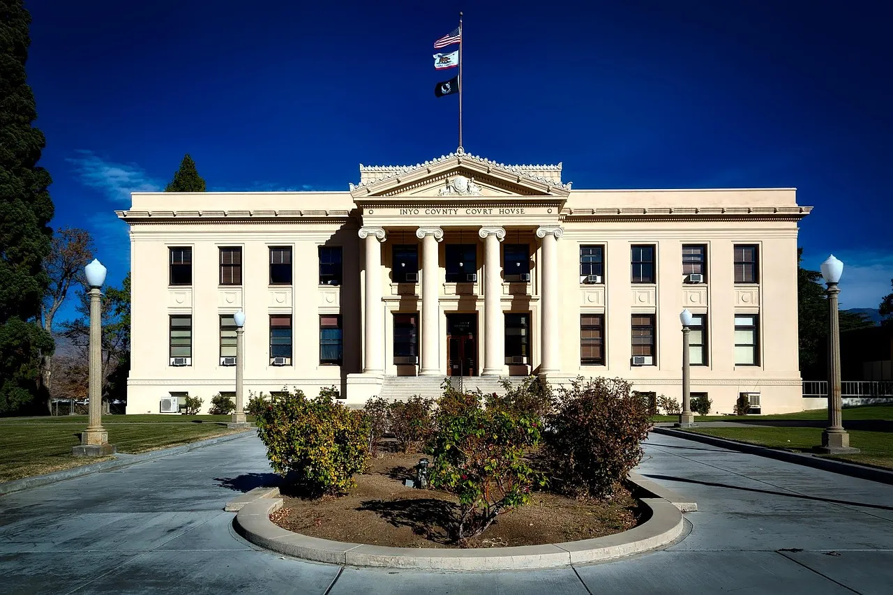 A white American county courthouse with columned entrance, flying the US and California state flags against a deep blue sky