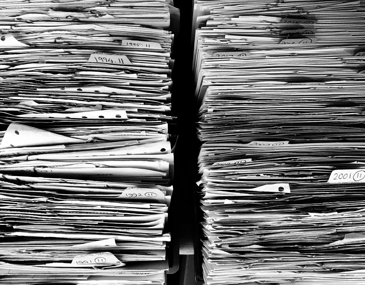 Two towering stacks of labelled paper files with handwritten date tabs on their edges — illustrative of a monthly patch load large enough to be counted three different ways.