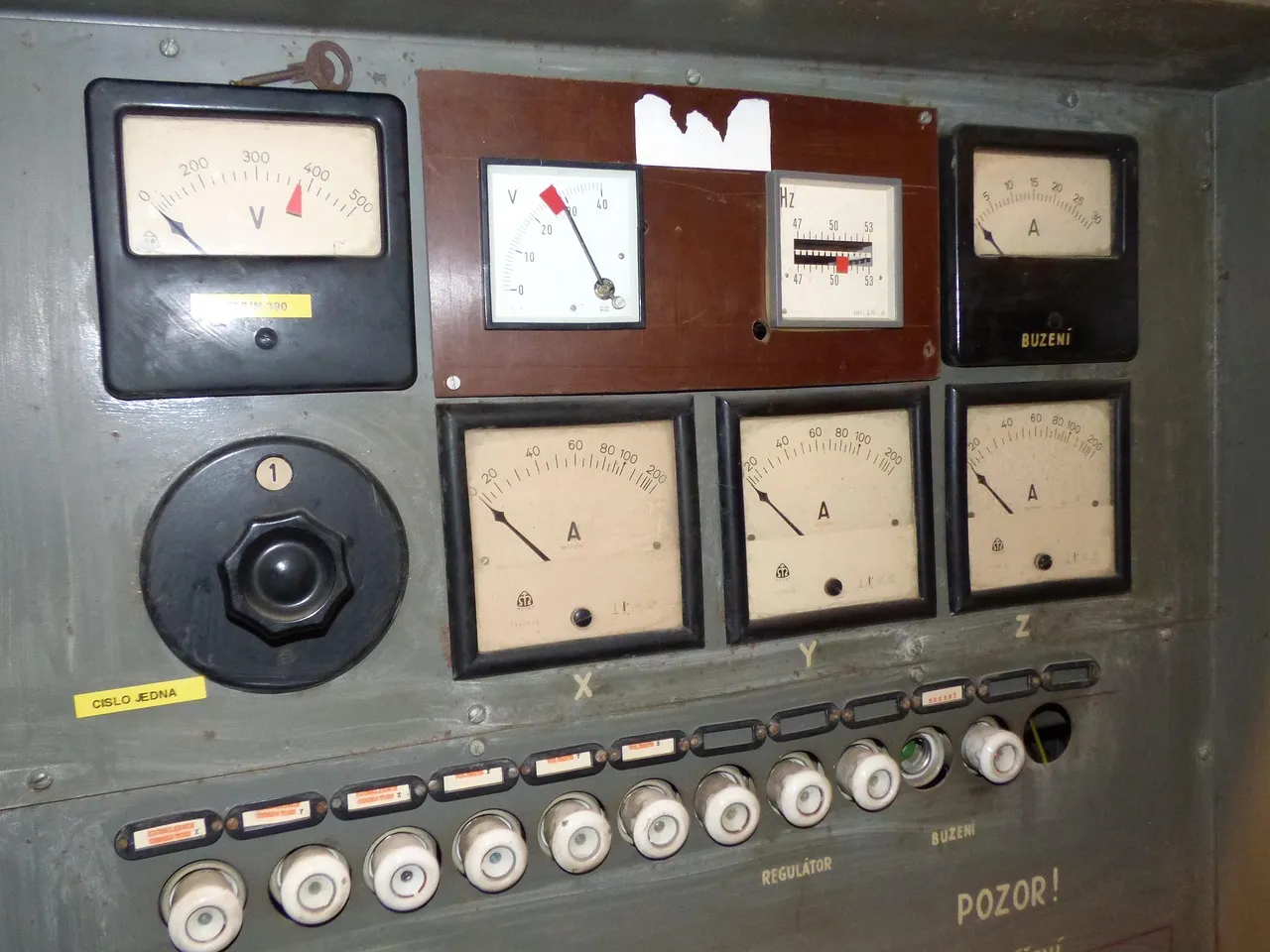 An old industrial control panel covered in analogue voltage and current dials above a row of switches