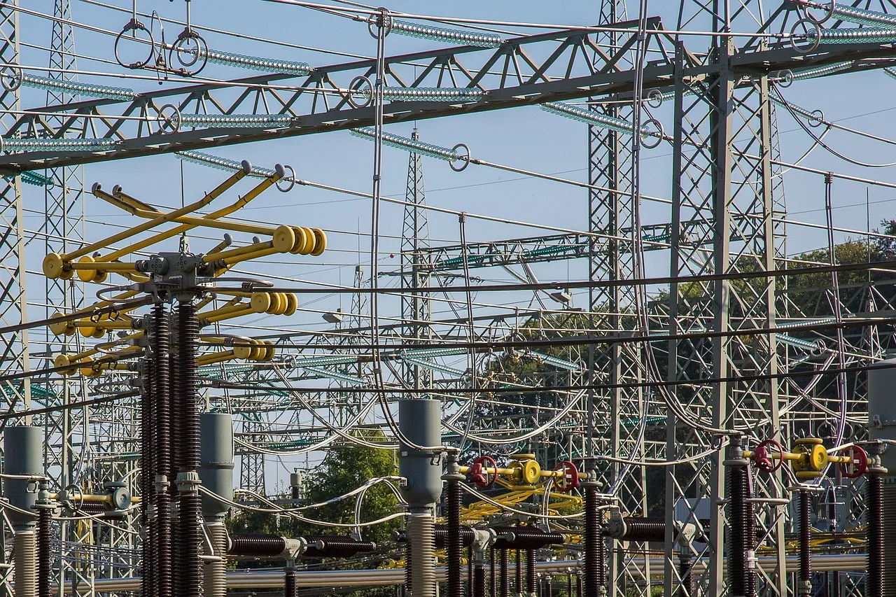 High-voltage switchgear, ceramic insulators and steel gantries inside an electricity substation switchyard.