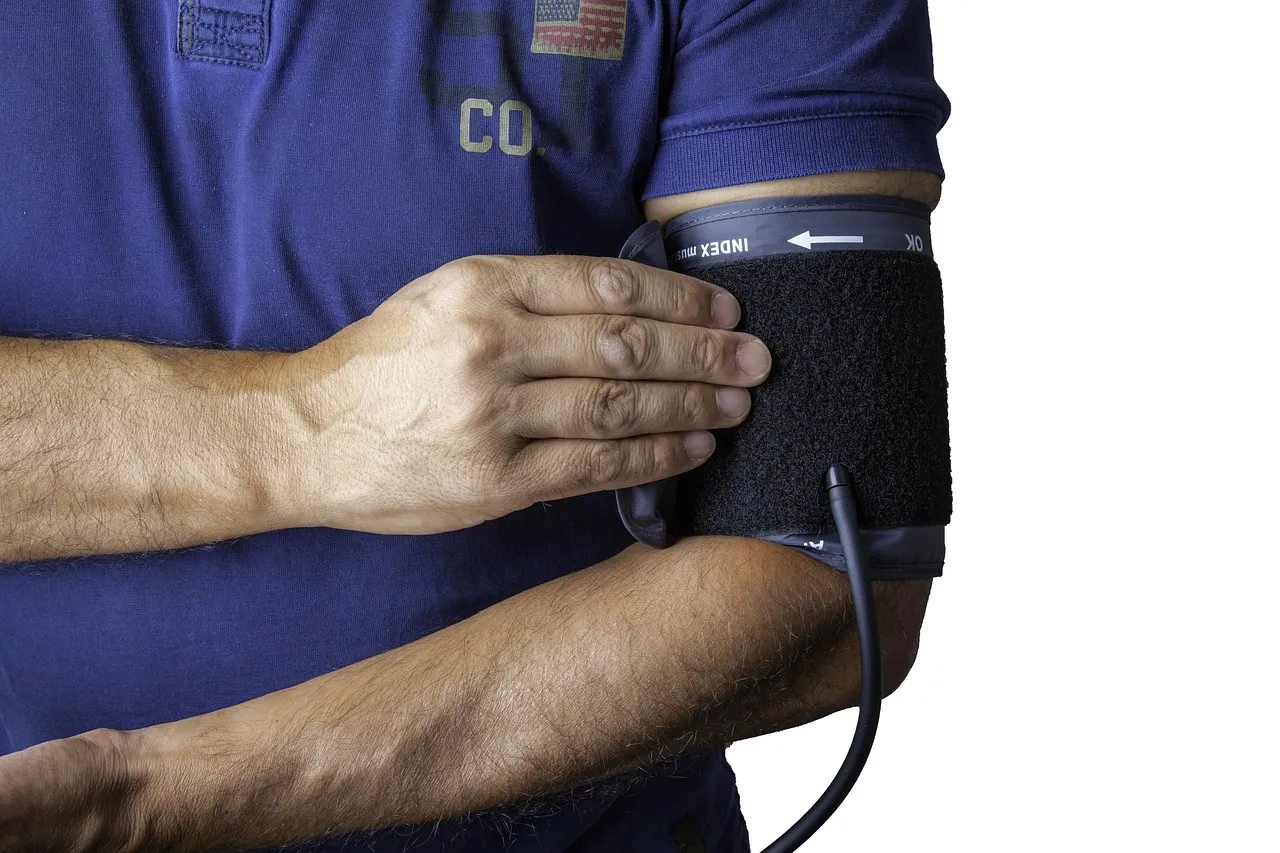 A man's upper arm in an inflated blood pressure cuff, his other hand resting across it