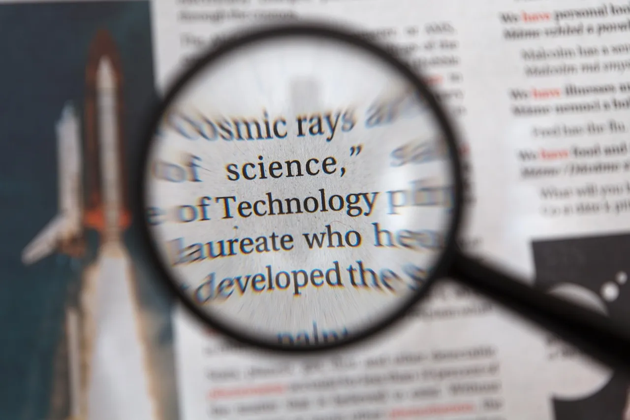 A magnifying glass held over a page of newsprint, enlarging a few words out of the surrounding text.