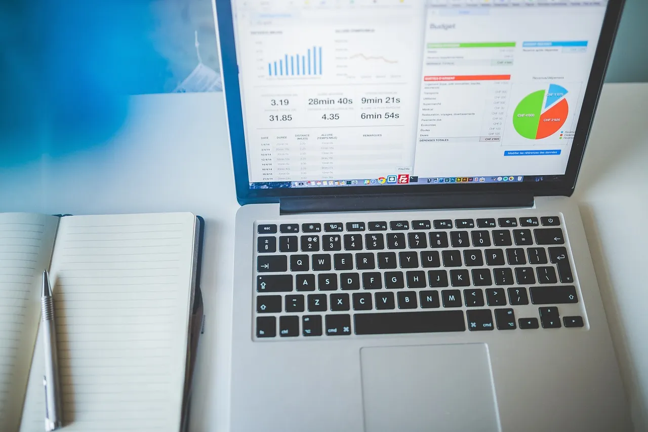 A laptop showing an analytics dashboard beside a notebook
