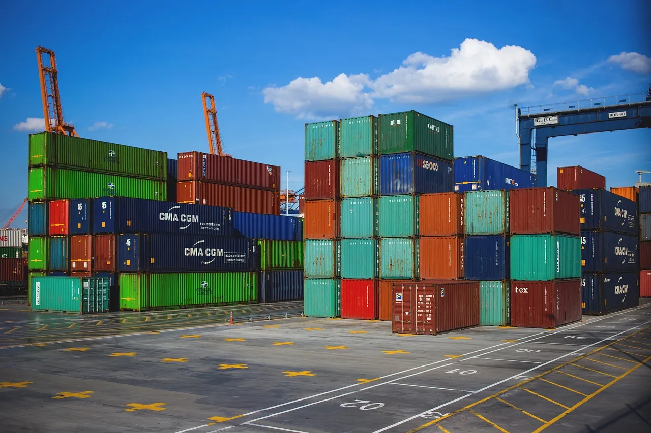 Stacked shipping containers beside gantry cranes at a port — illustrating the logistics contractor whose compromise reached several retailers' customers.