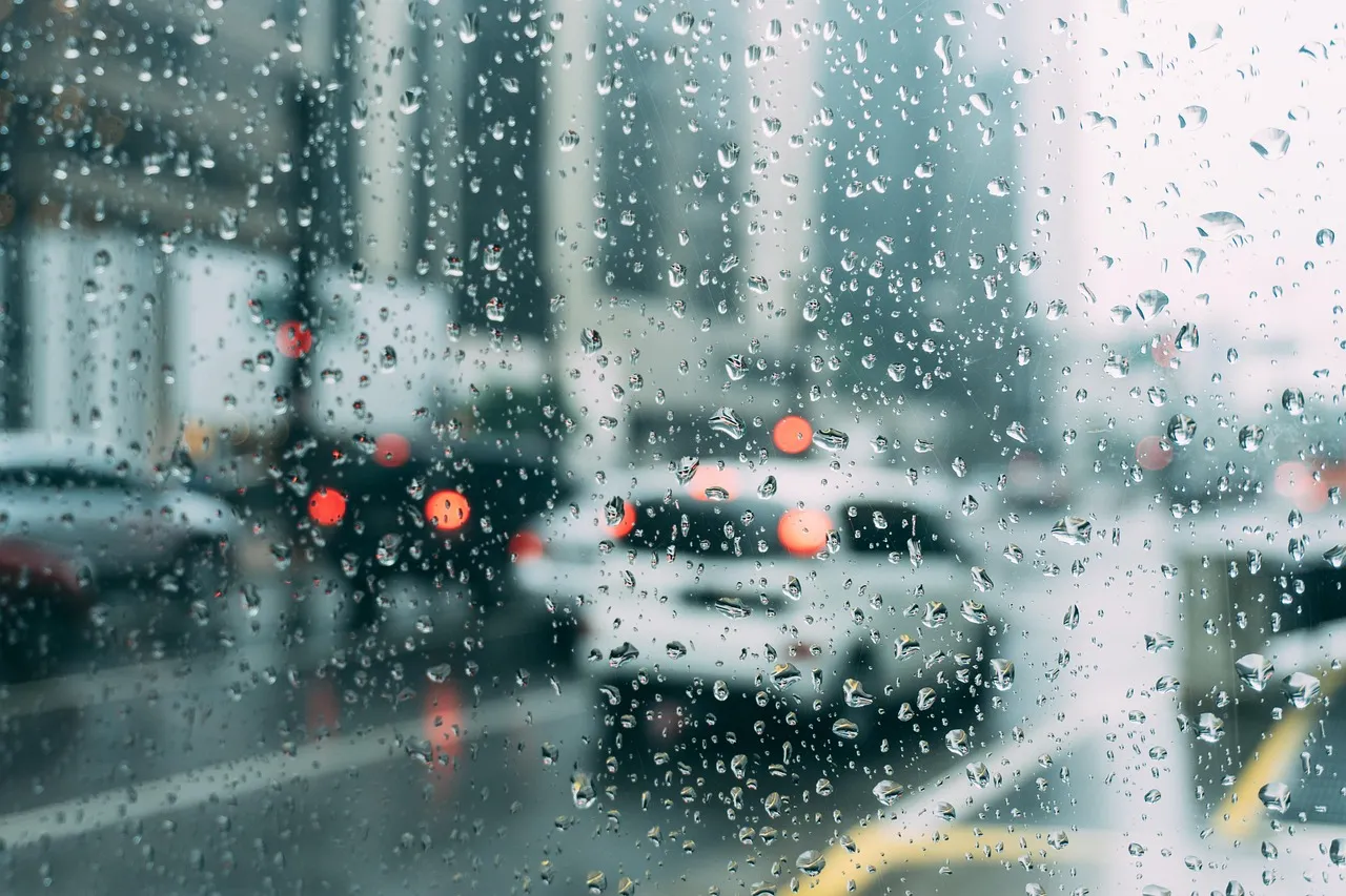 Raindrops on a windscreen with blurred cars and red brake lights ahead