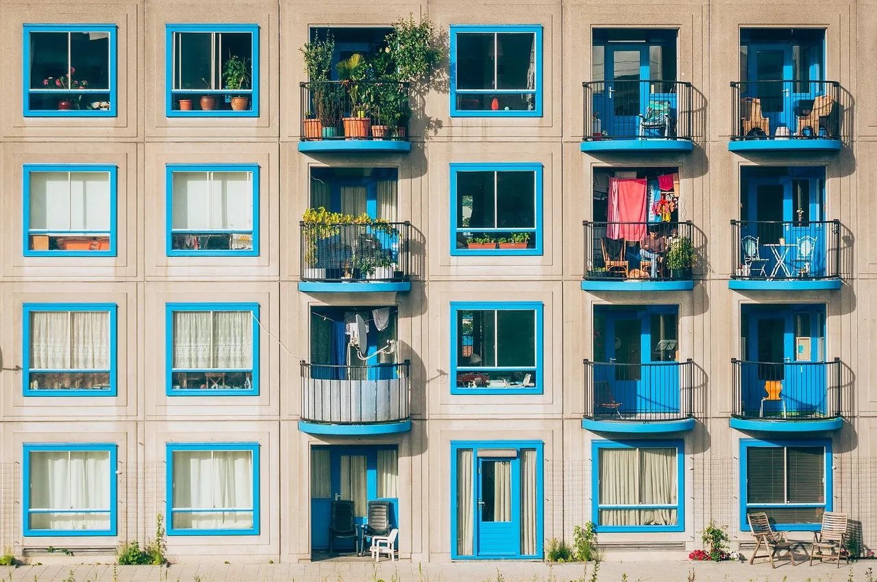 The facade of an apartment block, four storeys of near-identical windows and balconies with plants and laundry on several of them.