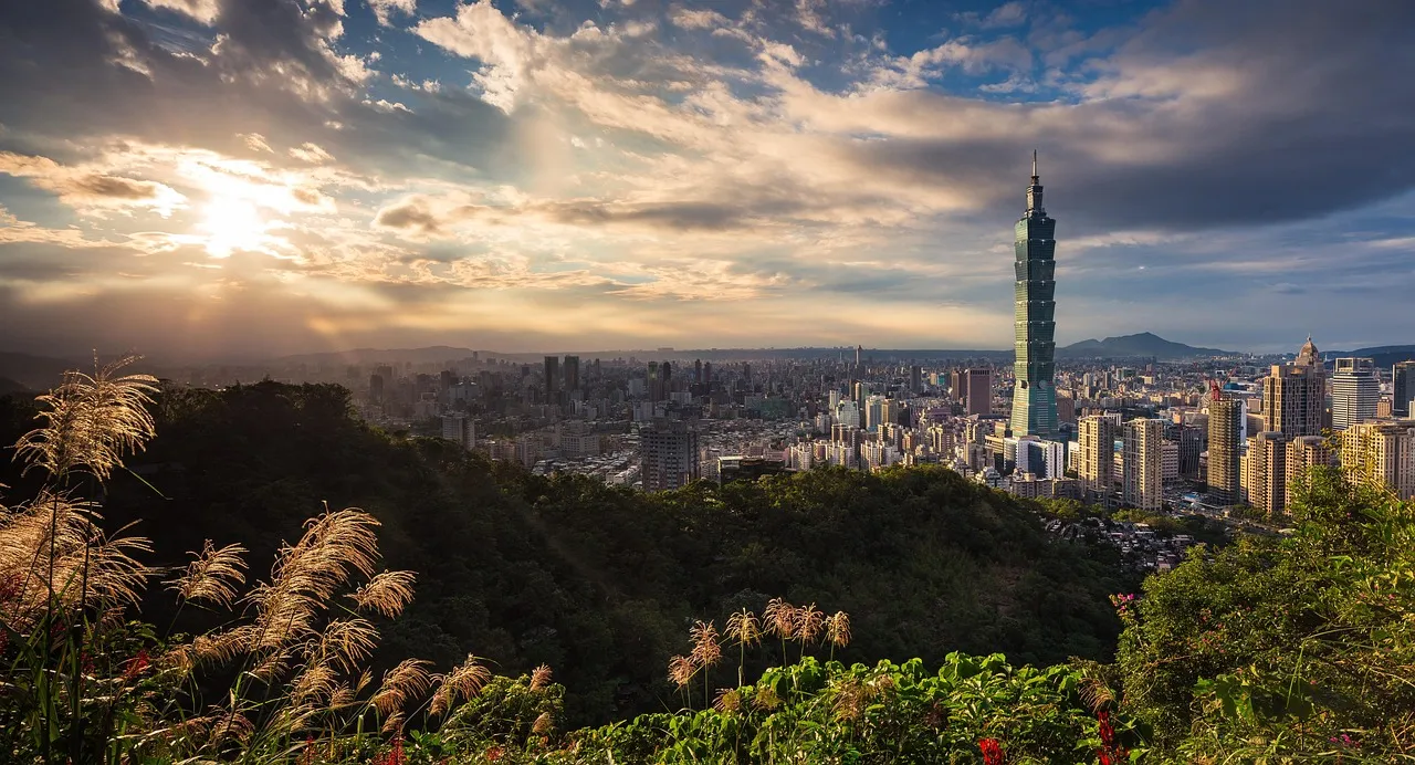 The Taipei skyline and Taipei 101 at sunset, seen from a wooded hillside