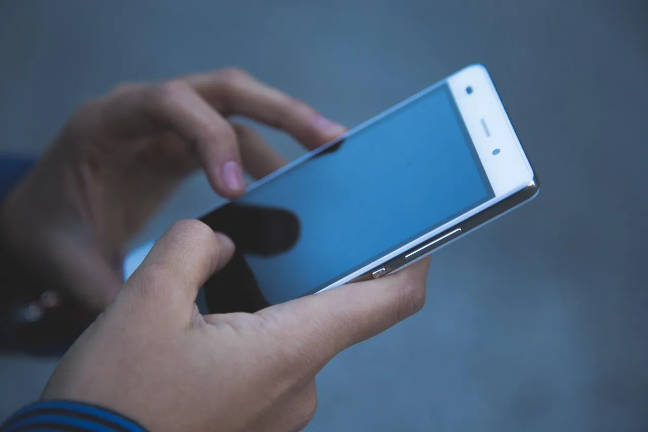 A pair of hands holding a smartphone with a blank screen, about to type