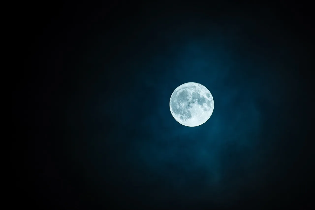 A full moon in a dark blue night sky, partly veiled by thin cloud