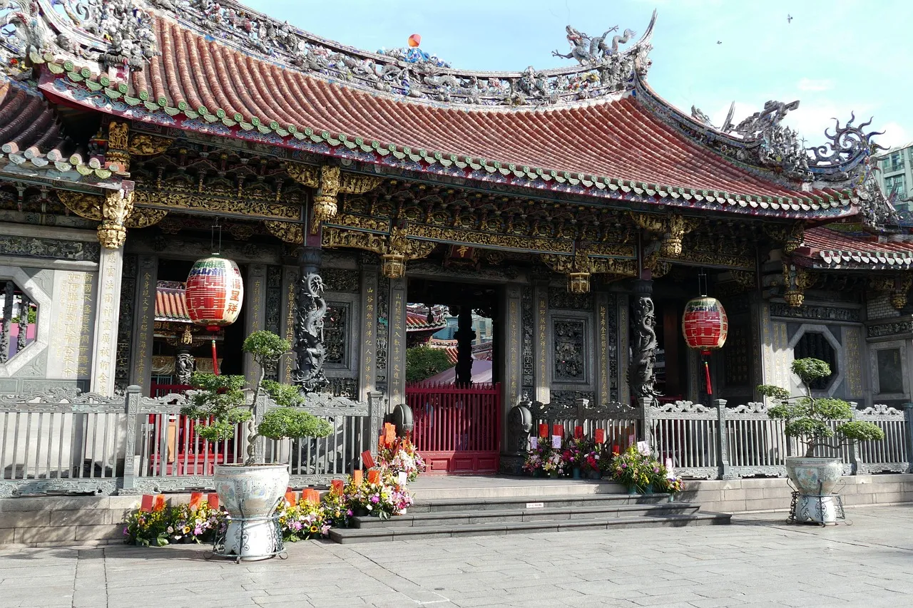 A temple hall with a curved red-tiled roof, carved dragons on the ridge and red lanterns at the doors