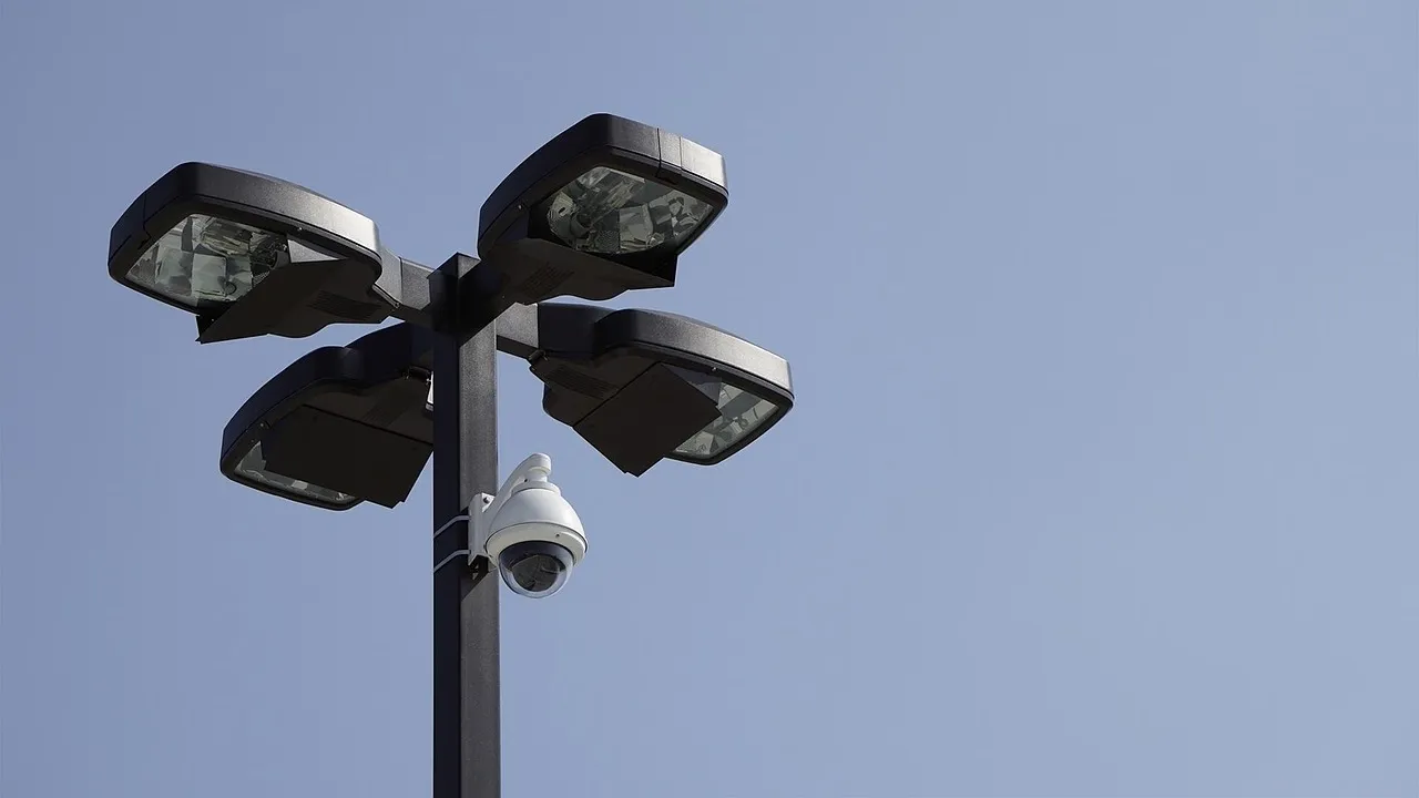 A dome surveillance camera mounted below the lamps on a street lighting pole