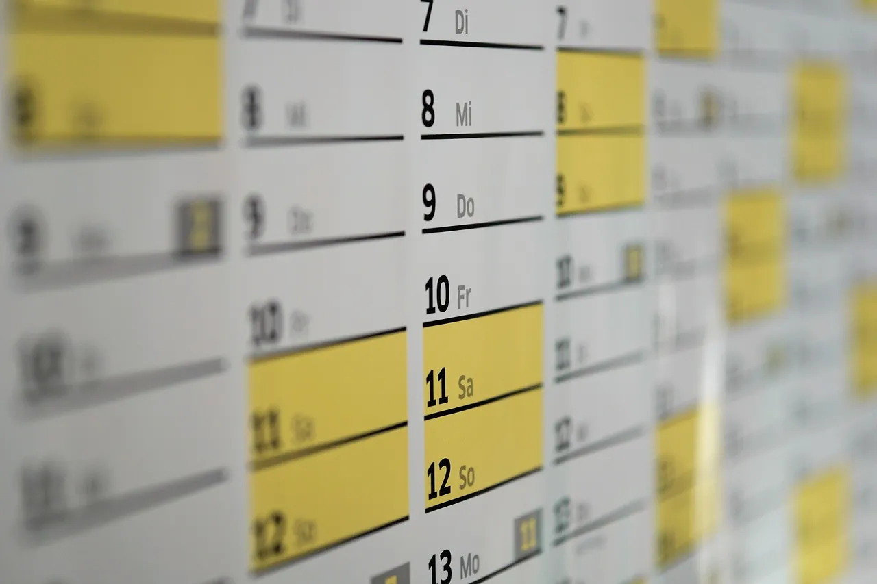 A wall-mounted year planner photographed in shallow focus, columns of printed date numbers running down the sheet with several rows blocked out in yellow highlighter.