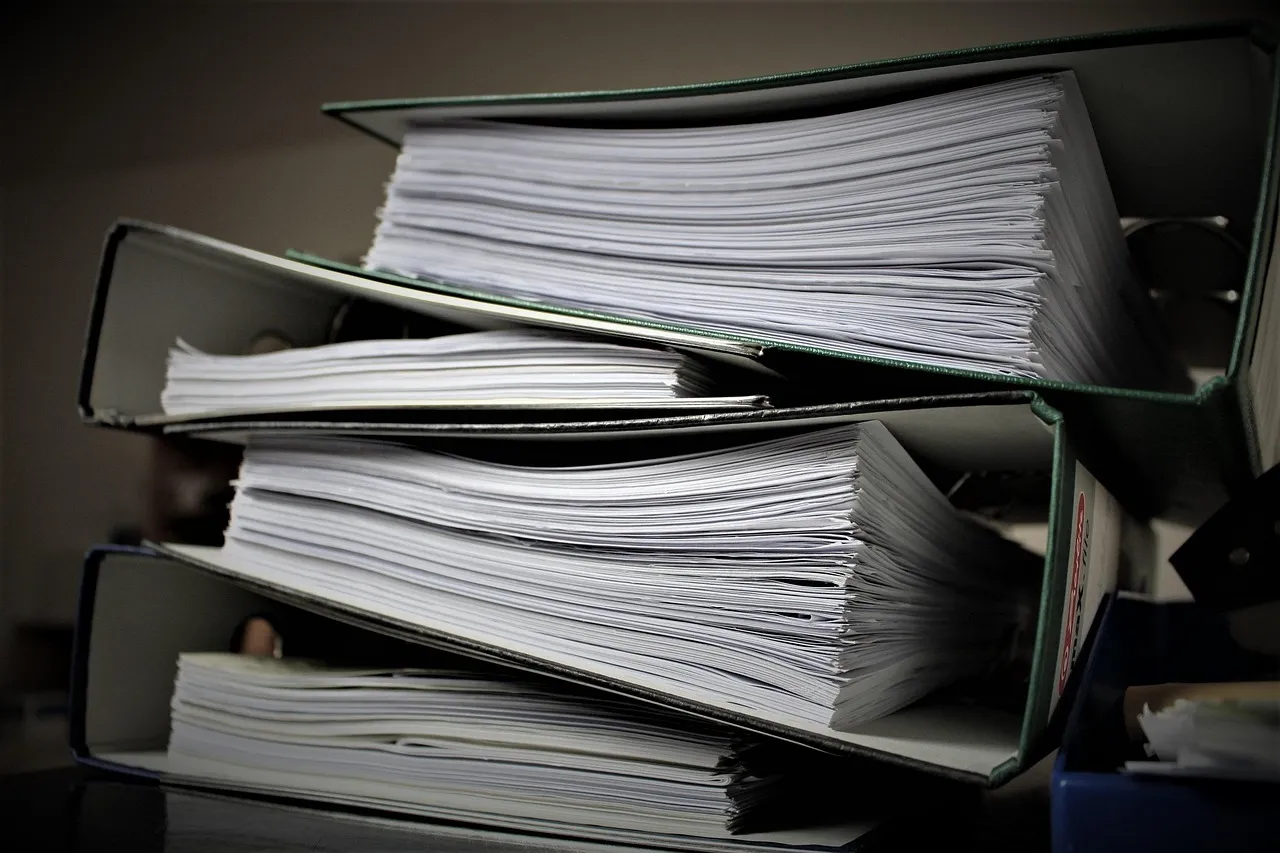 Three overstuffed ring binders stacked on a desk, each crammed with loose printed pages