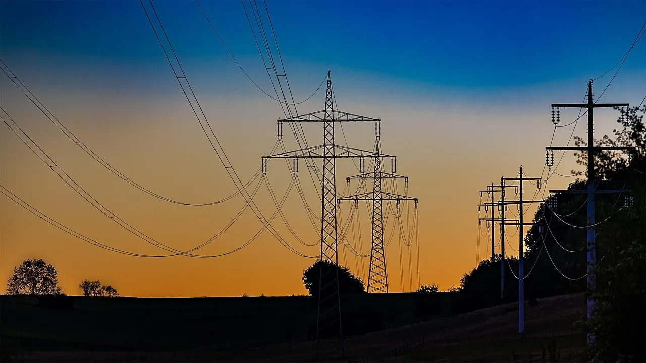 High-voltage transmission pylons silhouetted against an orange and blue dusk sky.