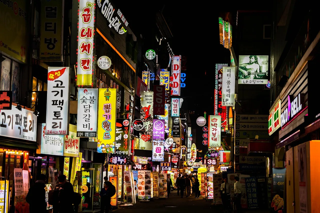 A night street in Seoul lined with illuminated shop signs in Hangul