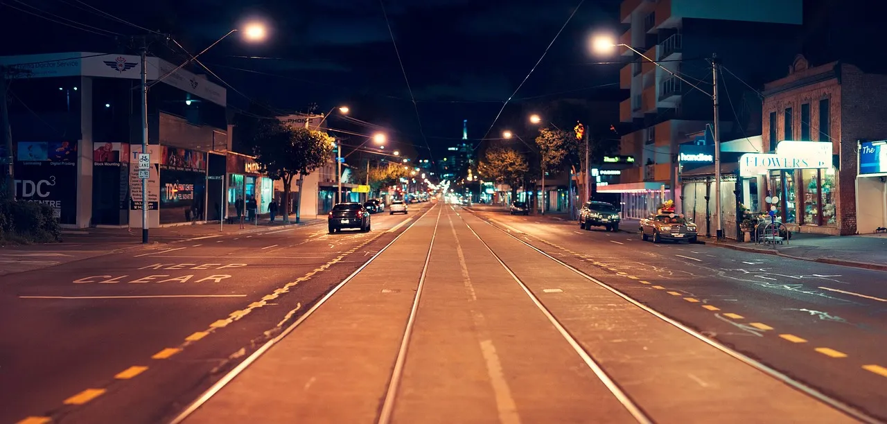 An empty city street at night, lit by streetlights, with tram tracks running down the centre