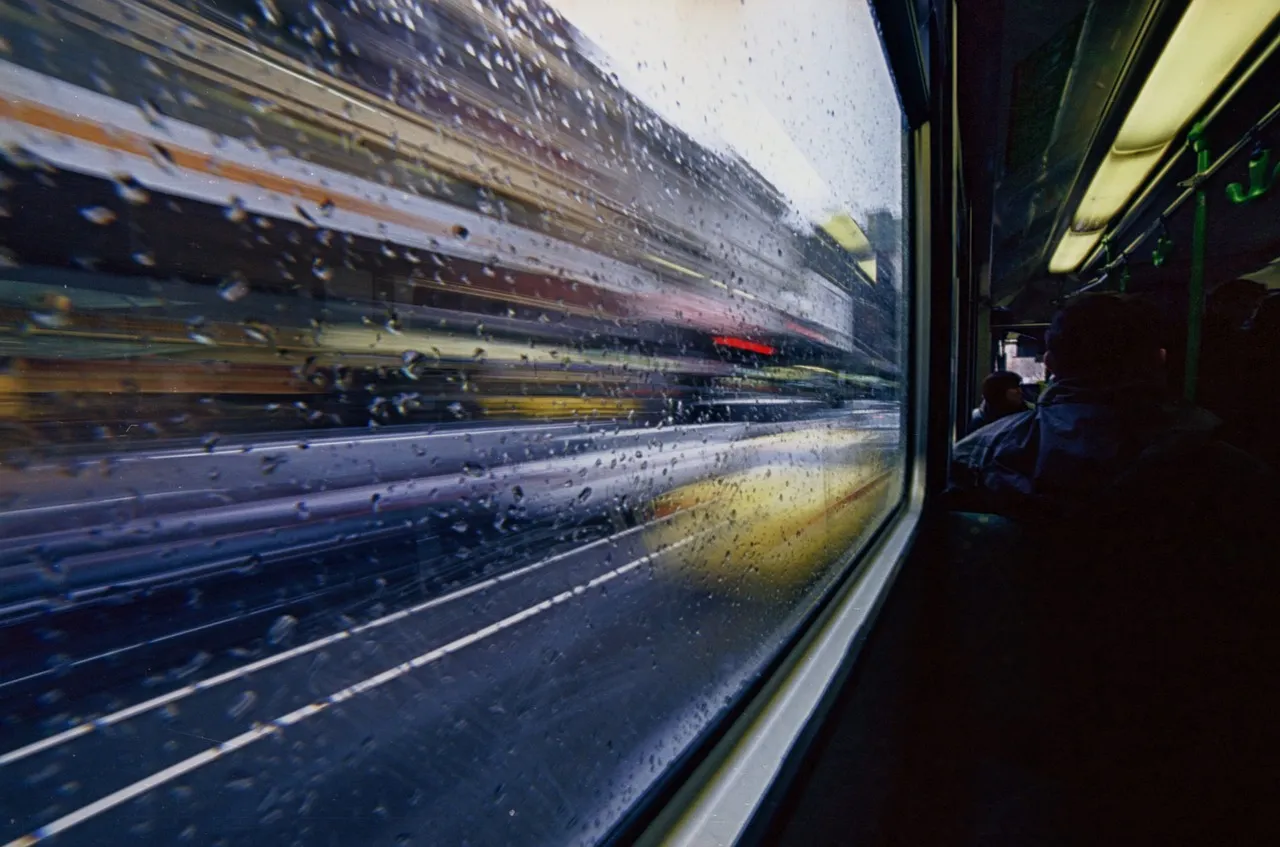 A rain-streaked tram window with the city blurring past outside