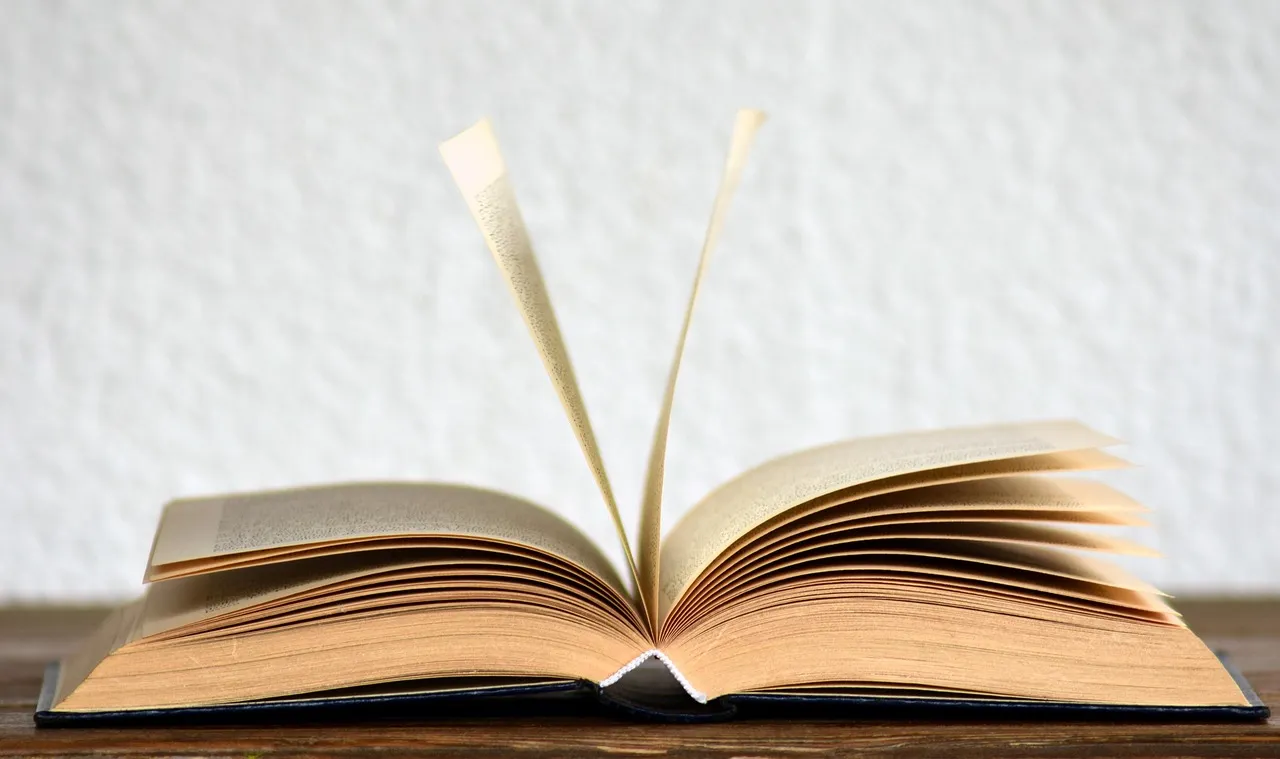 An open book resting on a wooden table with its pages fanned
