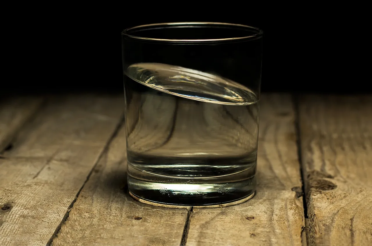 A half-full glass tumbler of clear water on a weathered wooden table