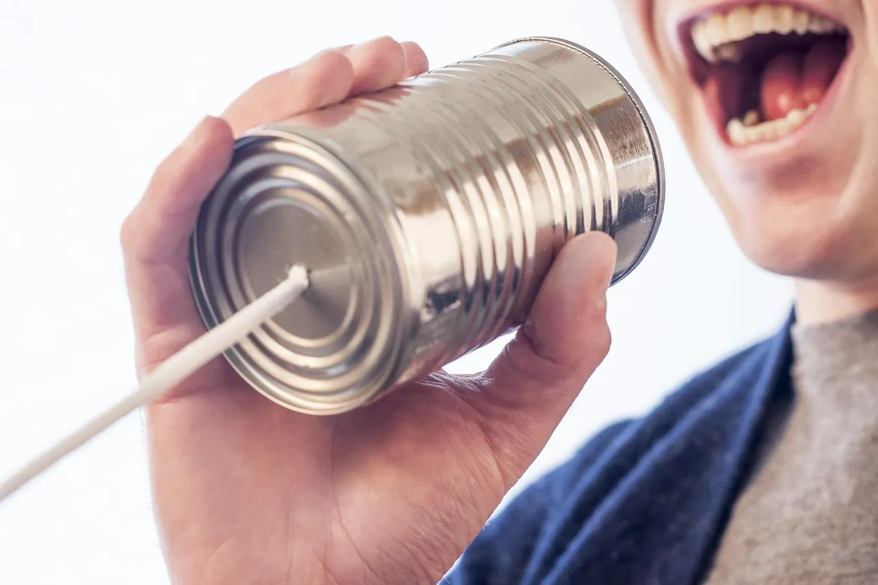 A hand holding a tin can to a speaker's mouth with a taut string running from its base, the simplest possible way to carry a message from one end to the other