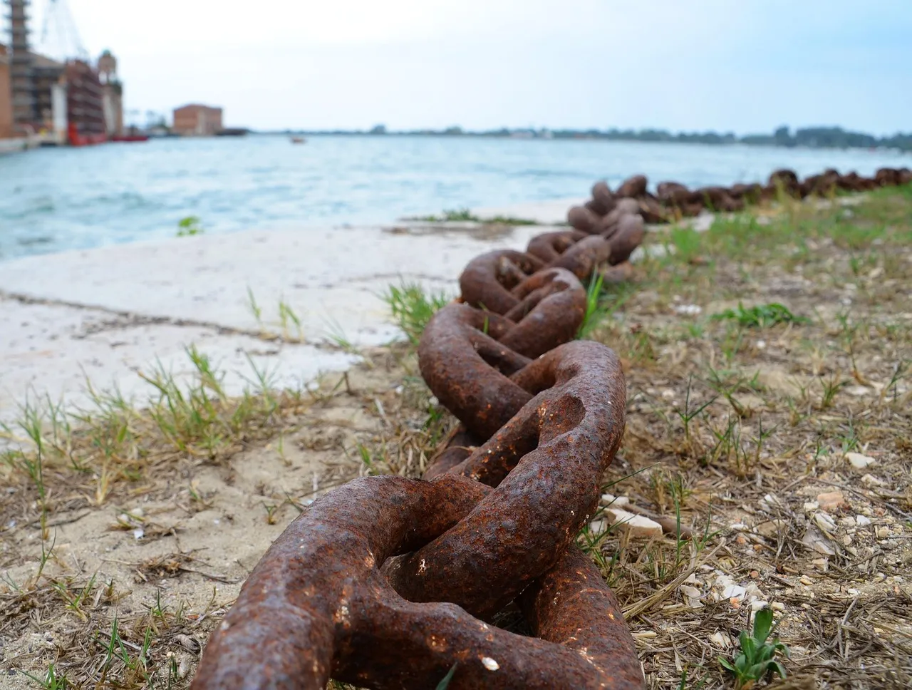 A heavy rusted chain of identical links running along a shoreline into the distance