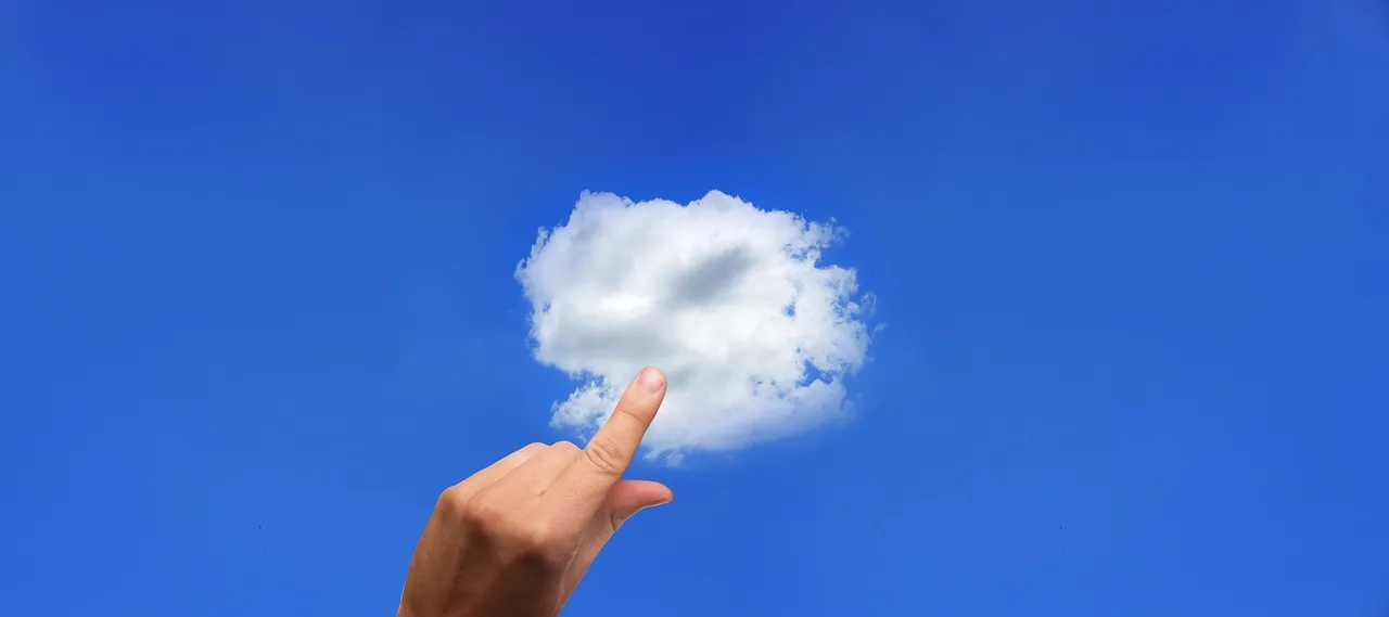 A hand reaching up to a small white cloud in a blue sky