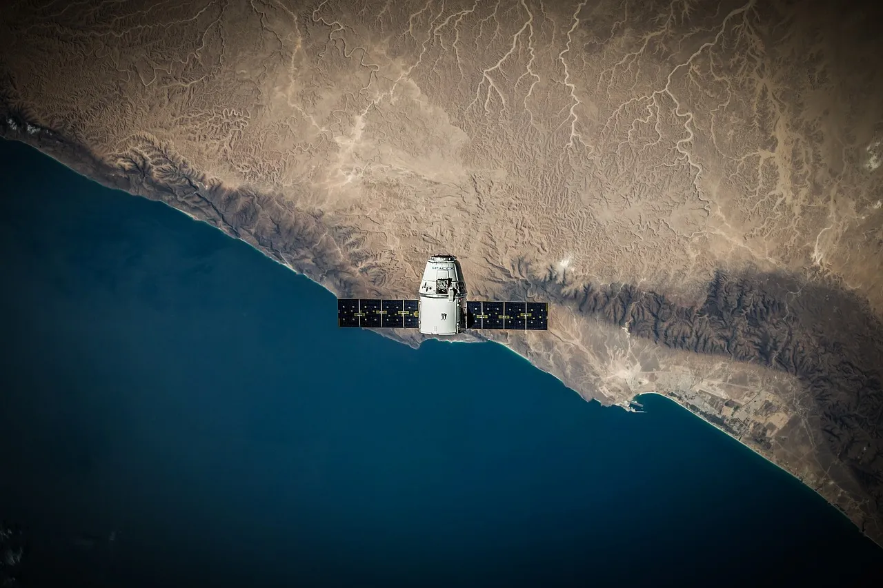 A spacecraft with solar arrays extended, photographed in orbit above a desert coastline — illustrative of an orbiting satellite; this is not MICHIBIKI No. 7.