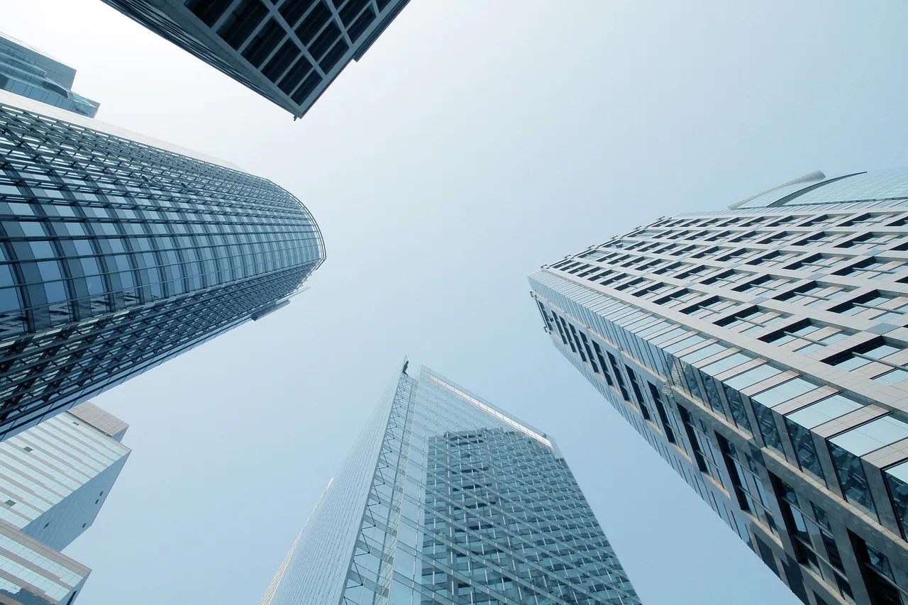 Glass and steel office towers photographed from ground level looking straight up into a pale sky