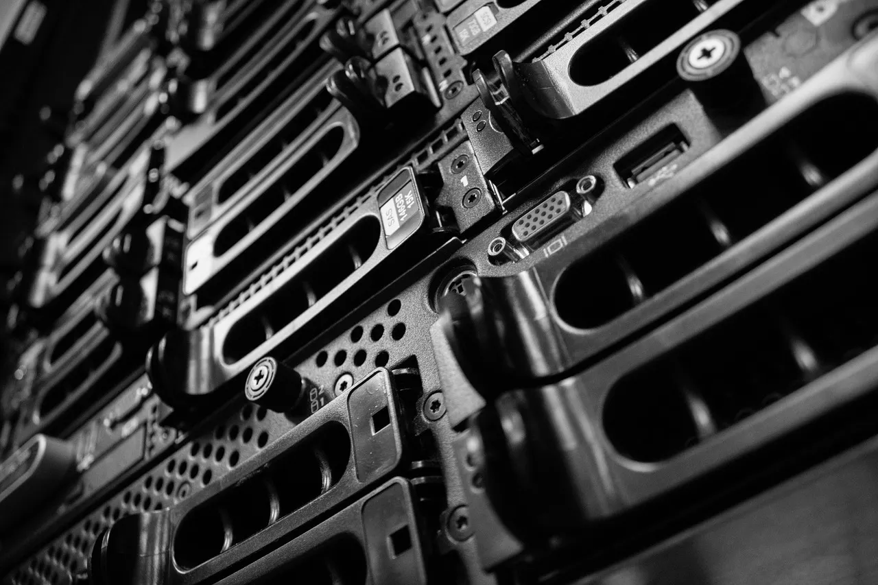 Illustrative: a monochrome close-up of rack-mounted servers, drive bays and ports receding into shadow.