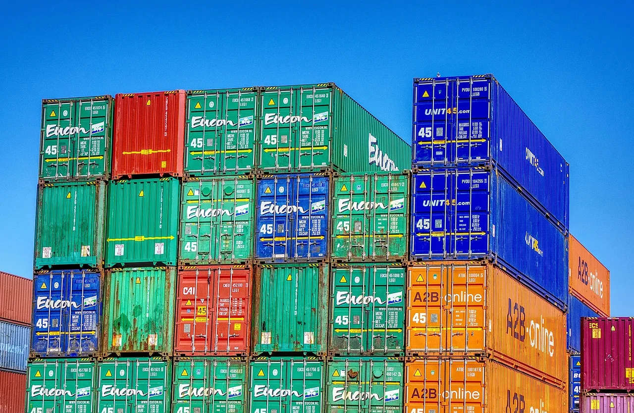 Rows of shipping containers in green, blue, red and orange stacked several high in a port yard against a clear blue sky
