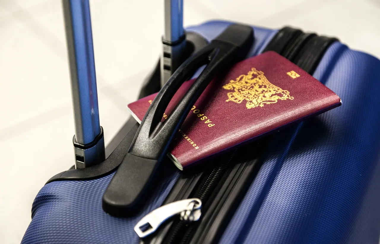 A passport resting on the handle of a blue suitcase