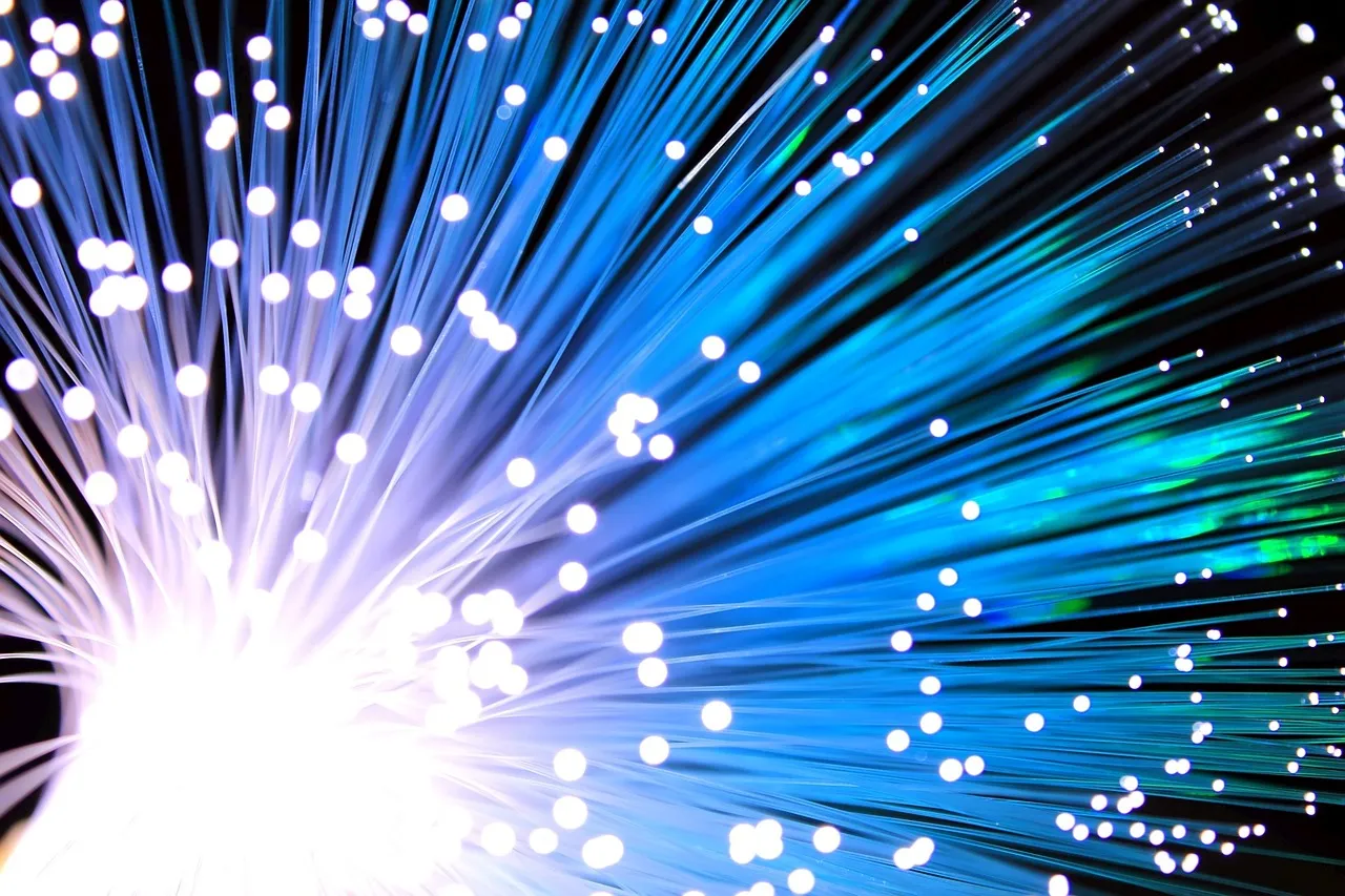 A dense spray of optical fibre strands with light emerging from their tips against a black background