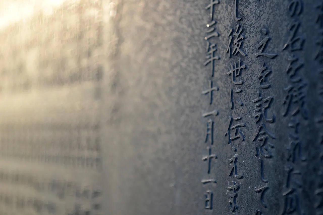 Rows of Japanese characters engraved into a pale stone surface, receding out of focus.