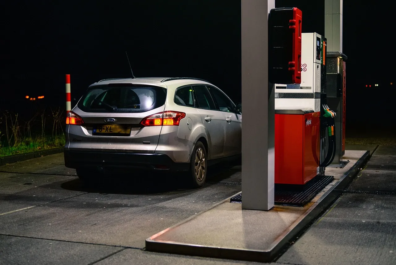 A car parked beside a filling-station pump at night, the pump unit lit in the foreground