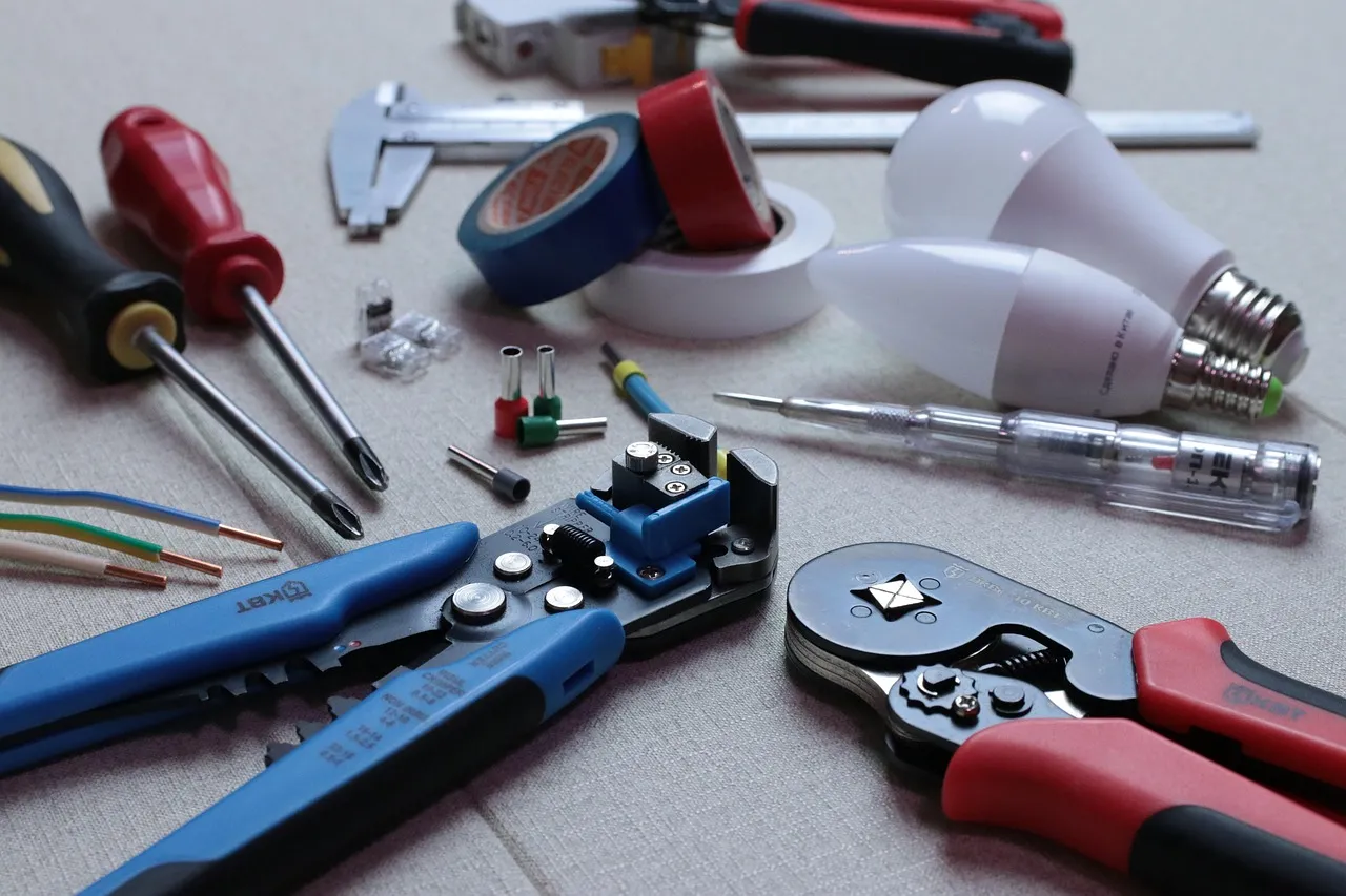 Electrician's tools laid out on a bench with a stripped three-core cable showing bare copper conductors.
